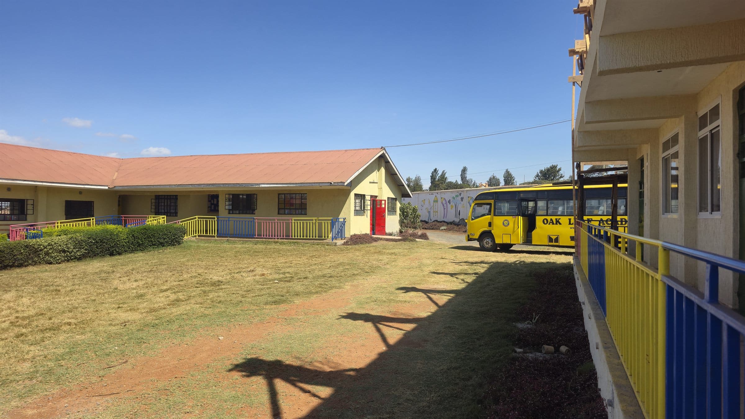 A wide view of the Oak Leaf Academy classroom block and green playing field, with the school bus at the far end.