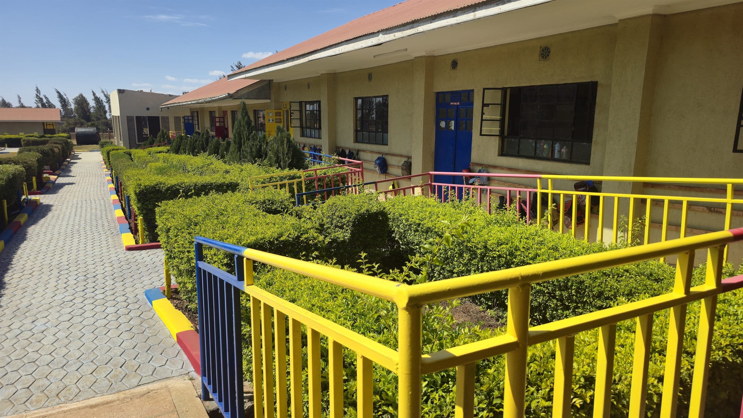 Neatly trimmed hedges and a yellow and blue safety railing outside Oak Leaf Academy classrooms.