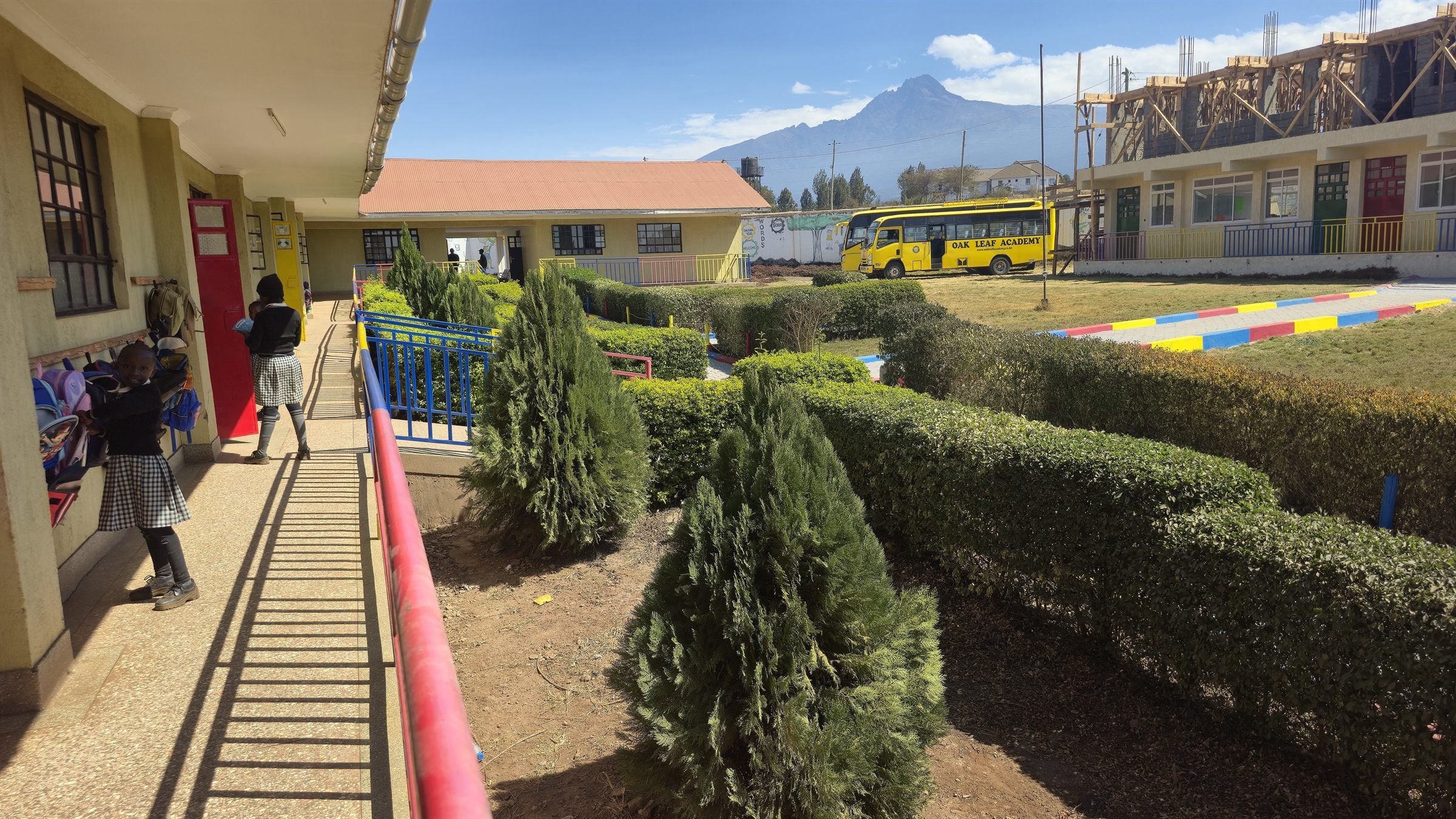 The Oak Leaf Academy campus in Nkama, Kajiado South, with brightly painted classroom blocks, landscaped grounds and the school bus, framed by Mount Kilimanjaro on the horizon.