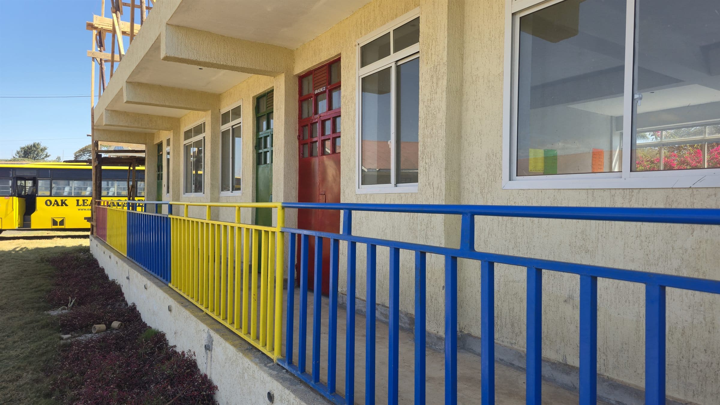 Colourful classroom doors and windows along the Oak Leaf Academy pre-primary block, with the school bus parked nearby.