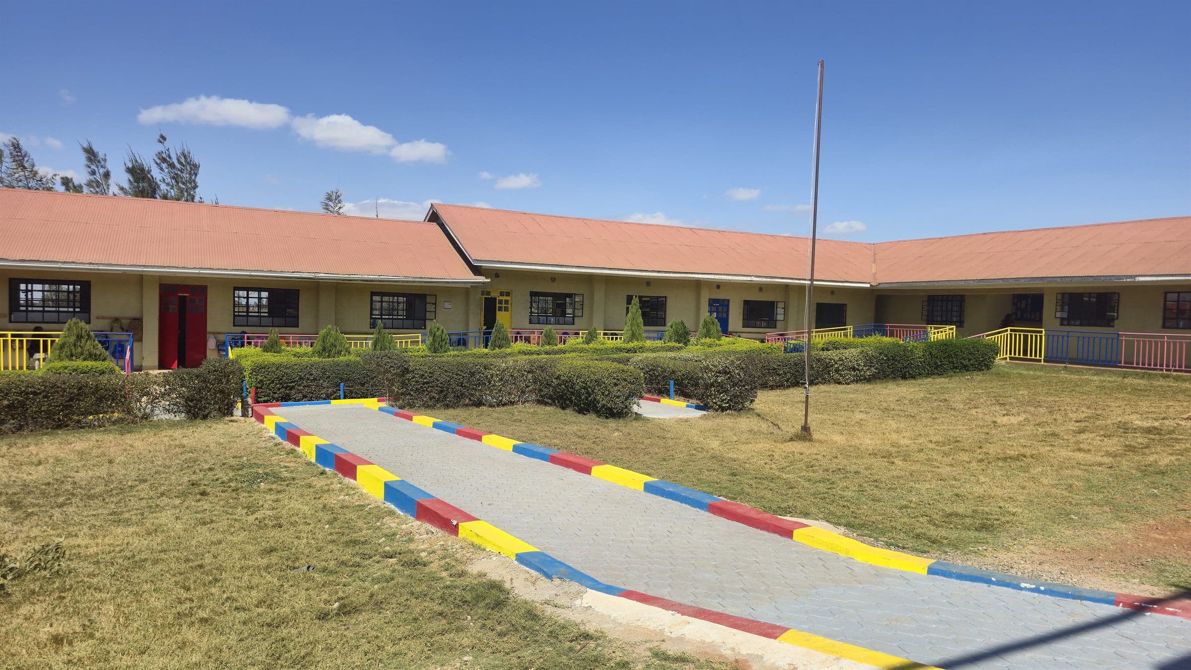 A paved, brightly kerbed walkway running the length of the Oak Leaf Academy classroom block, with lawns on either side.
